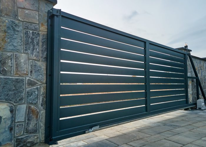 Wide automatic sliding gate with remote control installed in high stone fense wall. Security and protection concept.